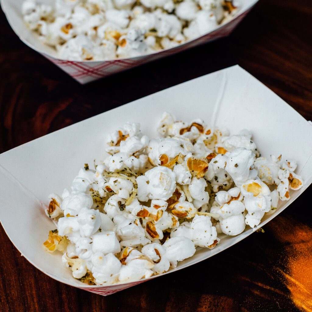 A paper boat filled with Smoked Parmesan Herb Popcorn.