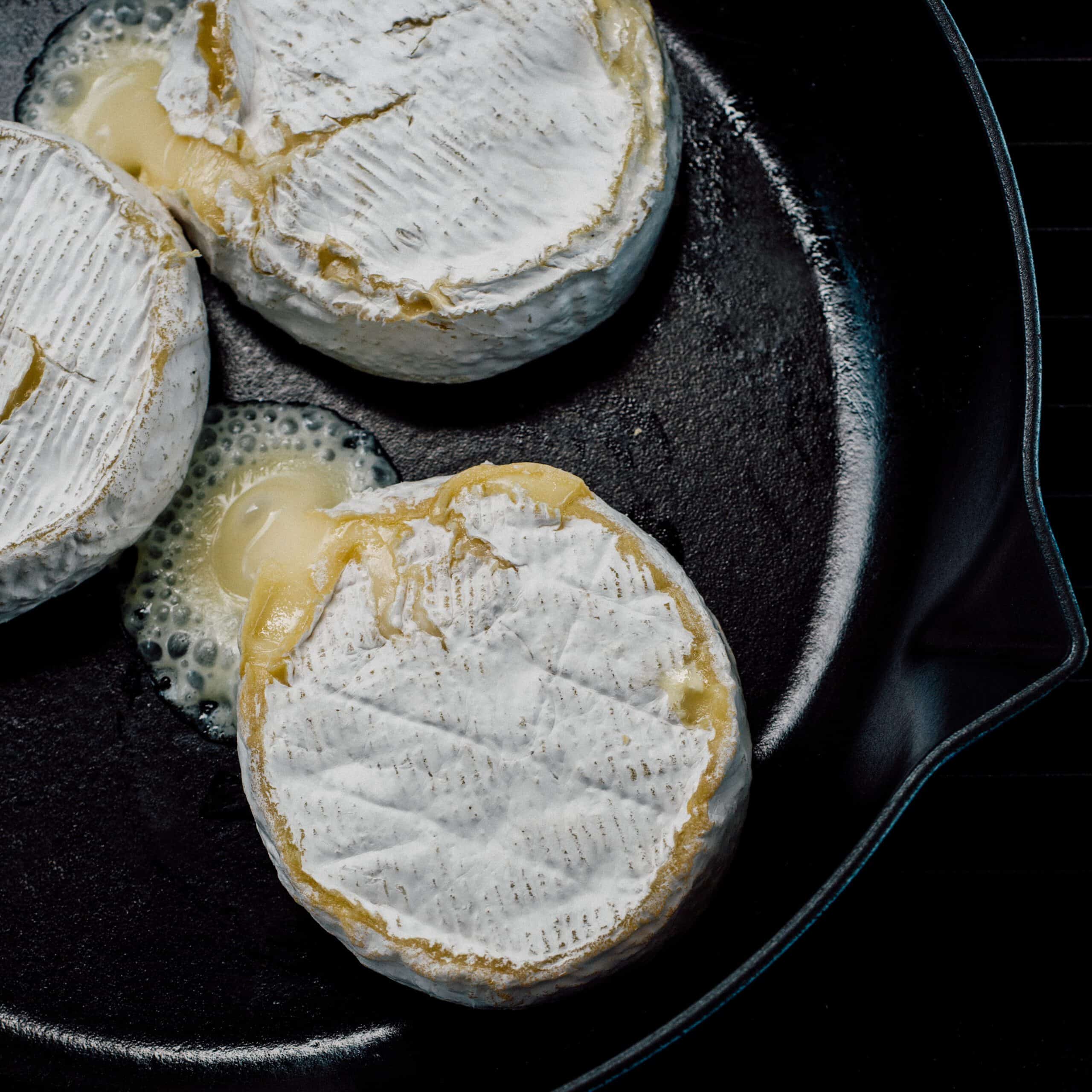 Three Brie wheels in a cast iron skillet, with oozing cheese.