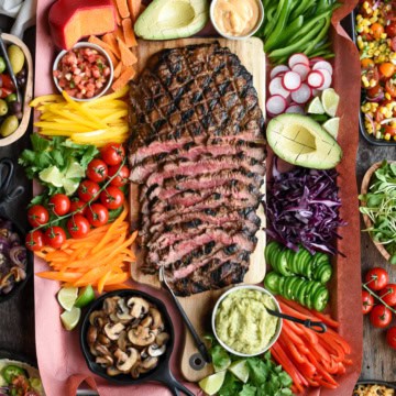 A spread of a sliced flank steak surrounded by an abundance of colourful toppings.