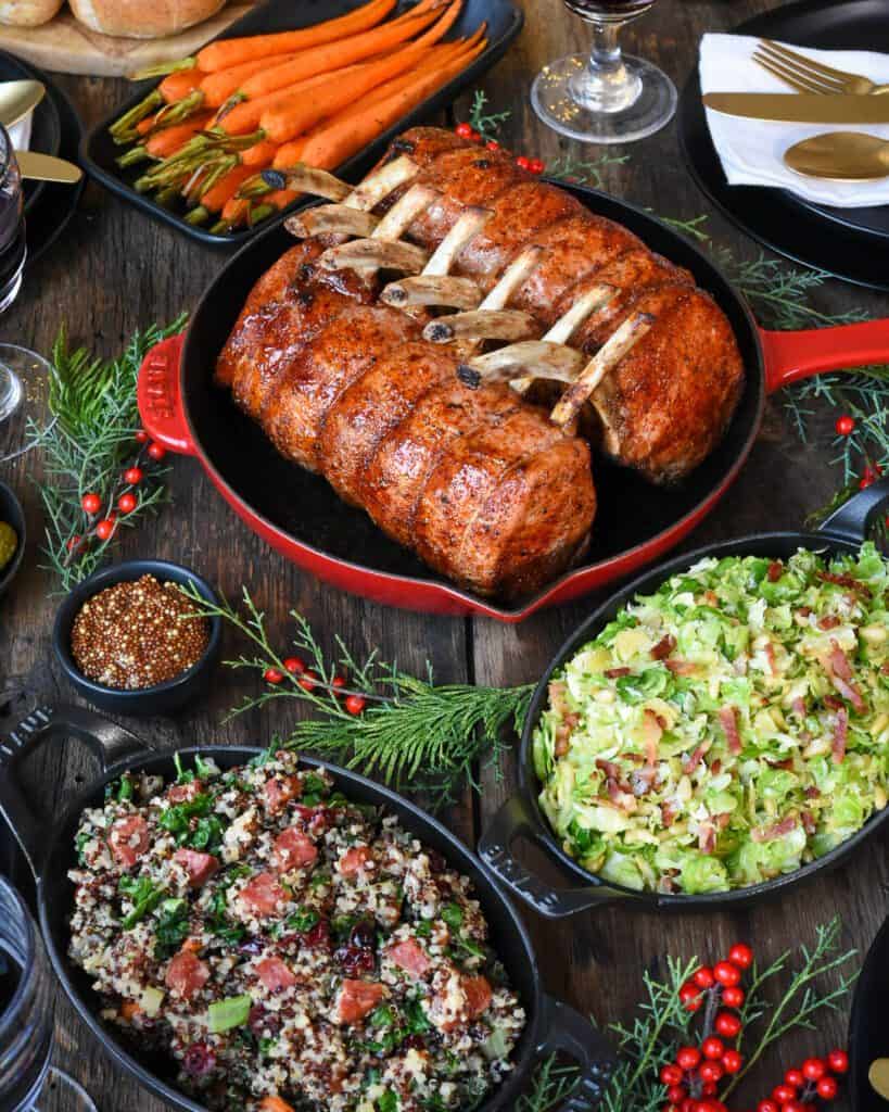Festive meal of two racks of pork with sides including a kale dish, a quinoa dish and glazed carrots.