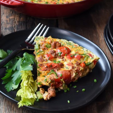 A slice of a hot Italian sausage frittata on a plate with a skillet in the background.