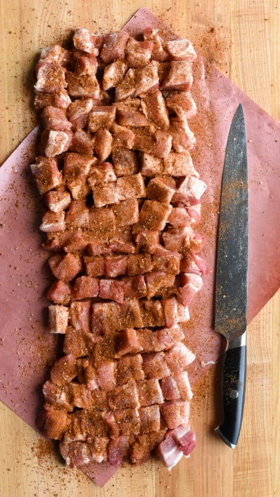 Cubes of pork belly seasoned on a piece of butcher paper with a large knife.