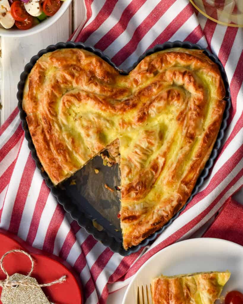 A Sausage and Feta Phyllo Pie rolled in coils and baked in a heart shaped pan. A slice is missing.