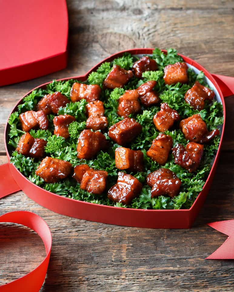 A red heart shaped Valentine's Day box with pork candy on a bed of parsley.
