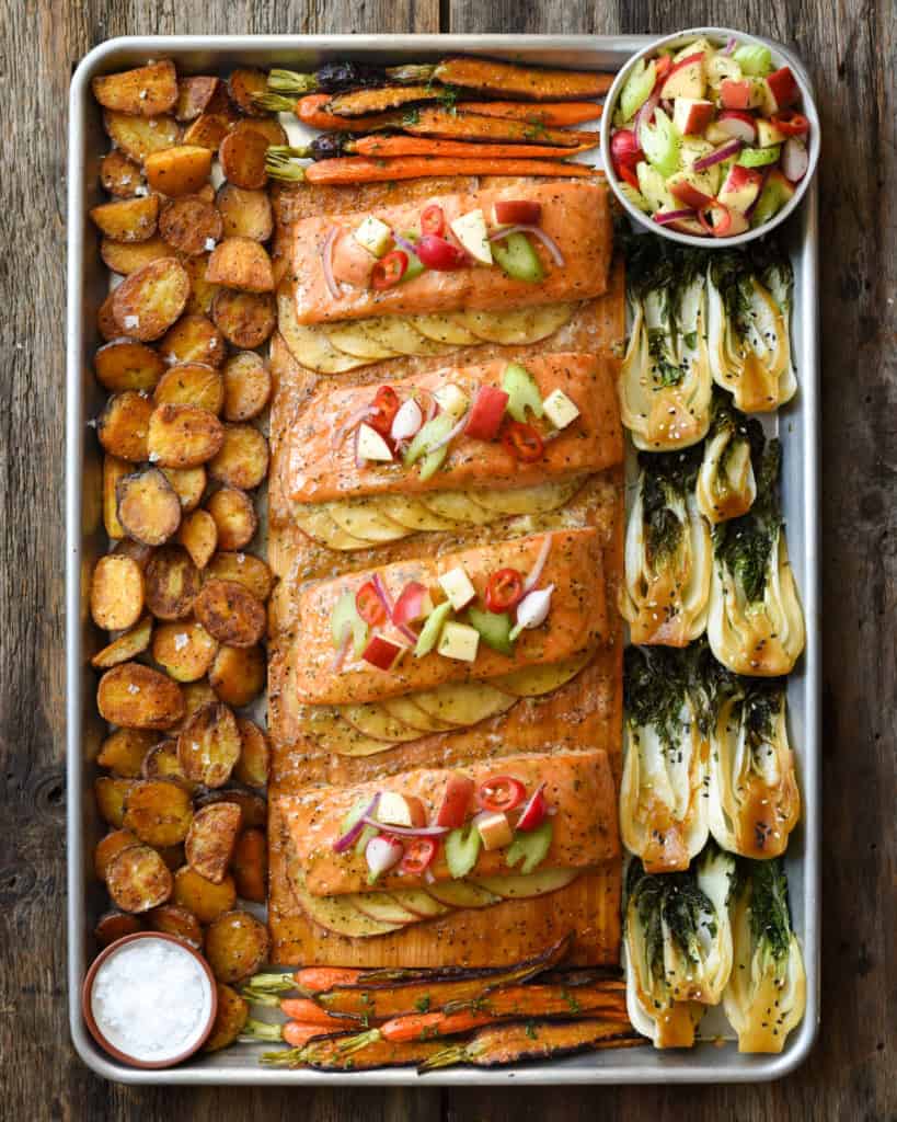Four portions of salmon on a cedar plank, served with apples, bok choy and potatoes.