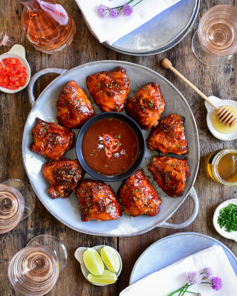 A round platter of Sweet-Heat Grilled Chicken Thighs served with a bowl of sauce.