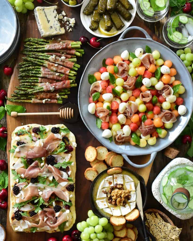 Large appetizer board with a Prosciutto and Mixed Melon Salad, Homemade Flatbread with Prosciutto, Poached Pears & Blackberries and Prosciutto Wrapped Grilled Asparagus.