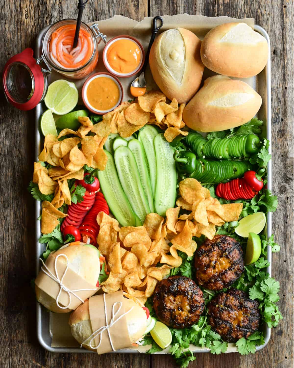 A large platter of buns, pork burger patties, fresh veggies, sauces and pickled carrots and daikons to make a Bahn Mi inspired burger.