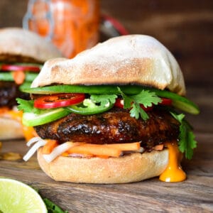 A side view of a Bahn Mi pork burger loaded with pickled and fresh vegetables and sauce on a French roll.