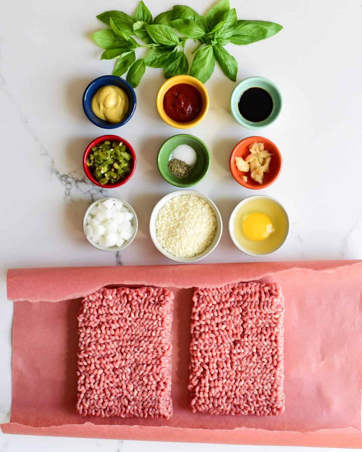 A top down view of ingredients for a pork burger which include nine small bowls of dry and wet ingredients and fresh ground pork.