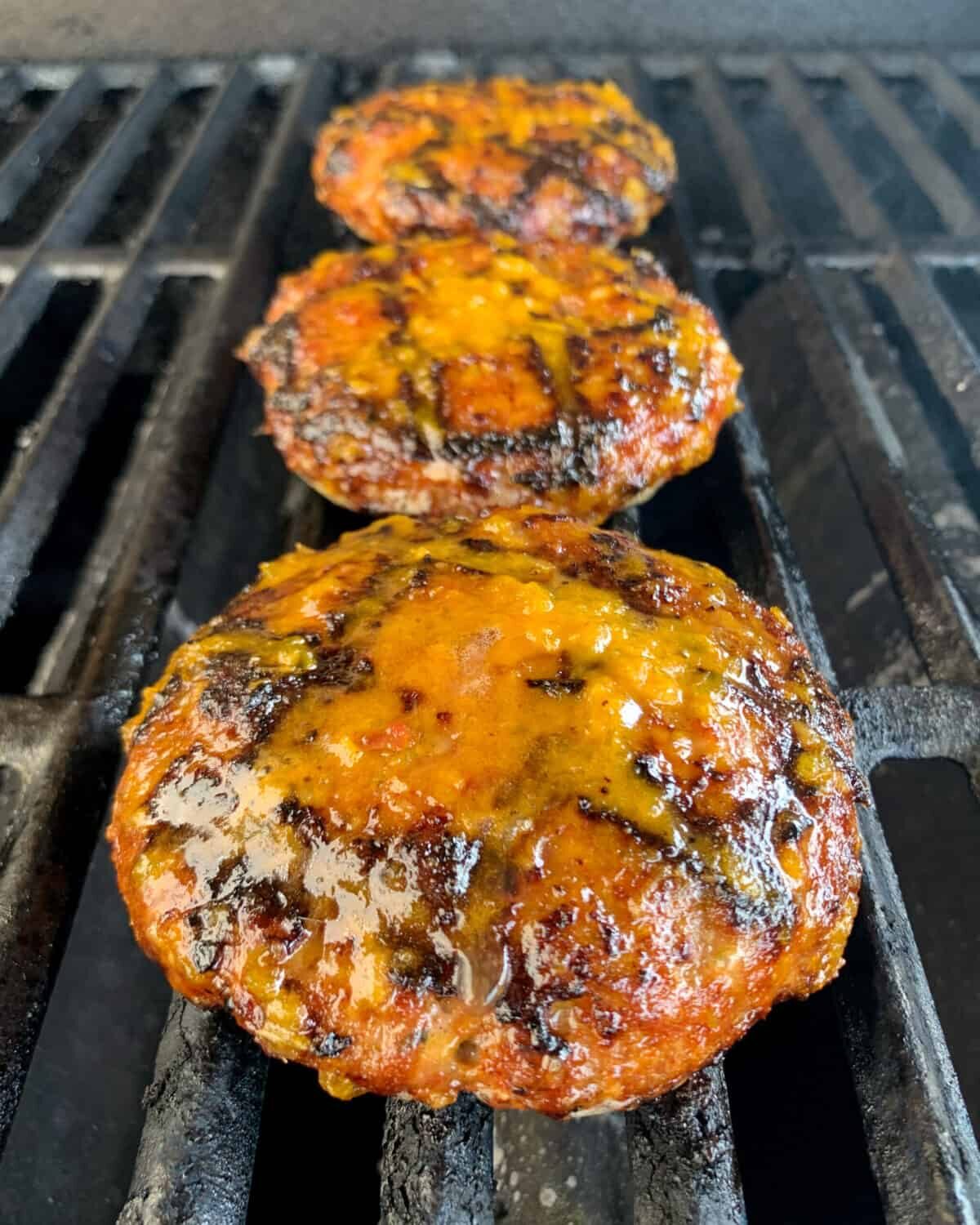Three burger patties on the grill with lemongrass pepper sauce.
