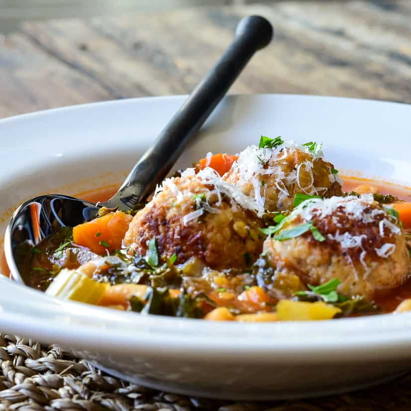 A side view shot of a bowl of meatball and pasta soup.