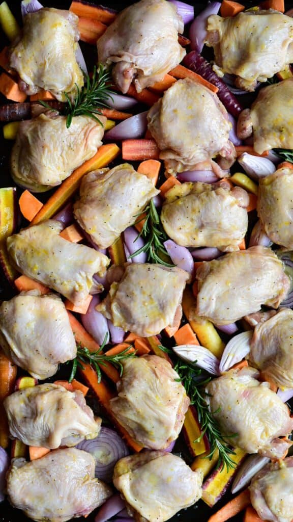 A sheet pan of veggies and chicken thighs ready to go into the oven