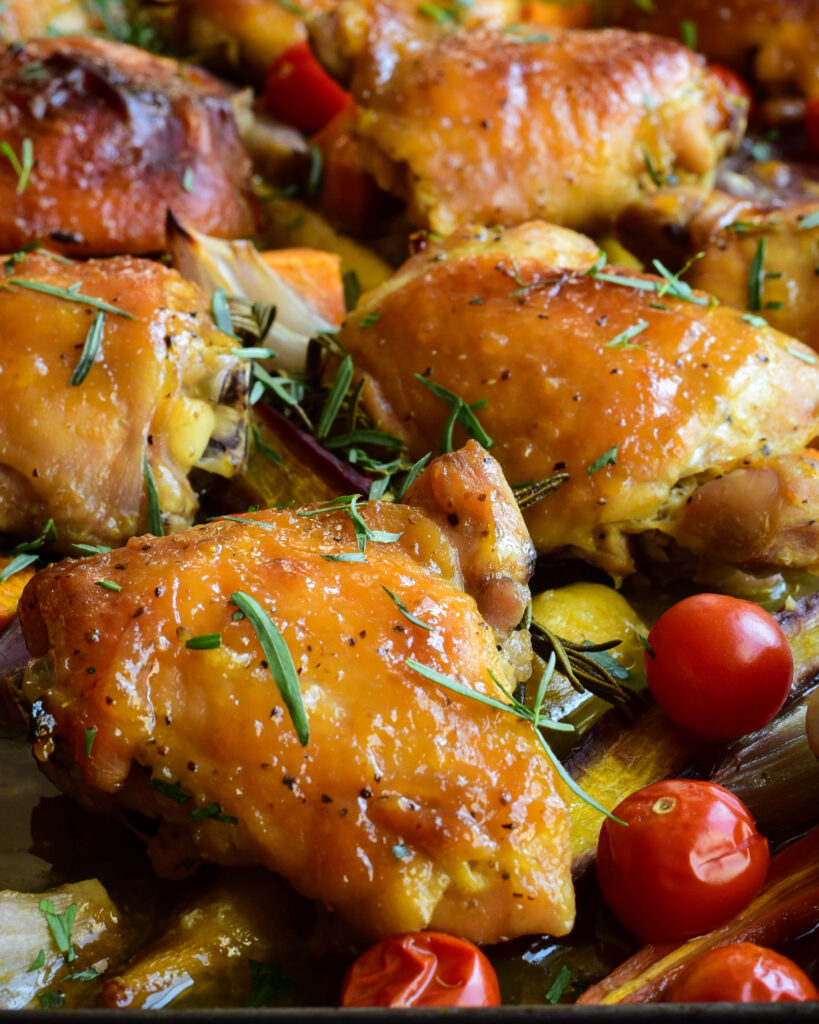Close up photo of a sheet pan of chicken thights with rosemary, taragon and veggies.