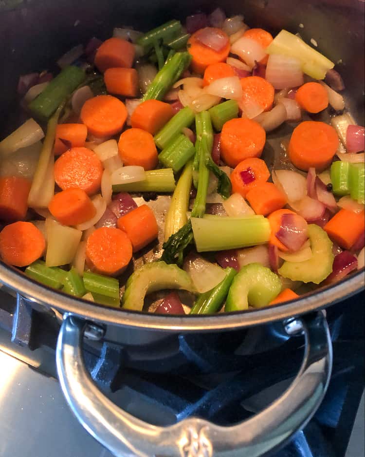 Chopped vegetables and peppercorns sauteing in a pan.