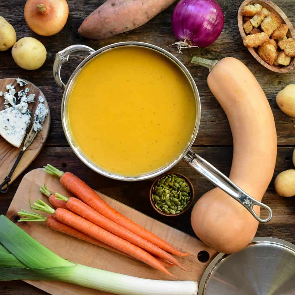 A pot of roasted vegetable soup surrounded by ingredients to make it.