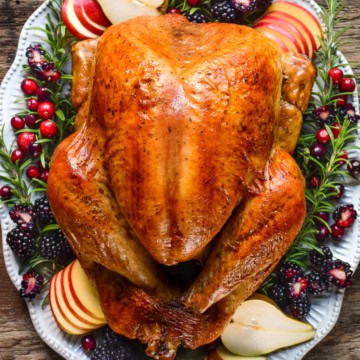 A golden, burnished turkey on a platter with garnishes.