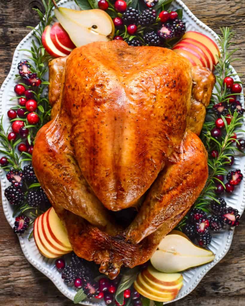 A golden, burnished turkey on a platter with garnishes.