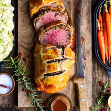A sliced beef wellington on a cutting board with a knife.