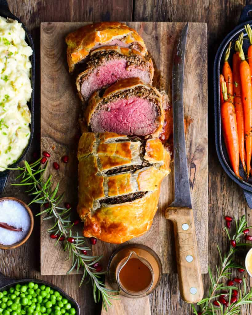 A sliced beef wellington on a cutting board with a knife.