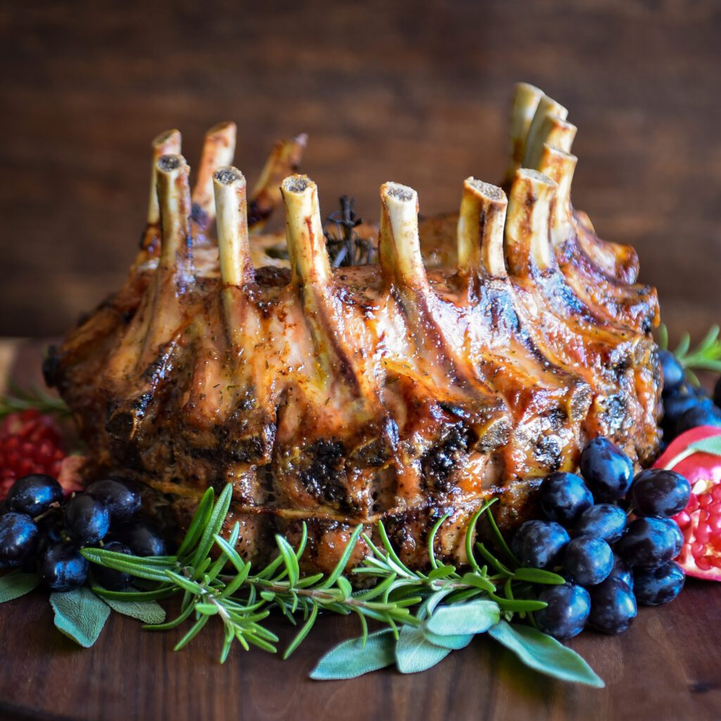 A grilled crown roast of pork decorated with herbs, grapes and pomegranates.