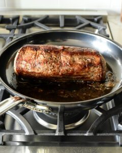 A beef tenderloin getting seared in a skillet.