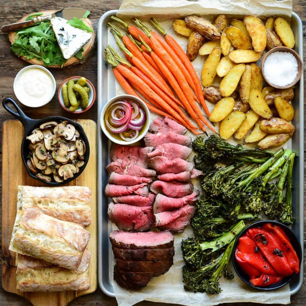 Roast beef dinner platter with carrots, potatoes, brocolini, roasted red pepers and sandwich fixings.