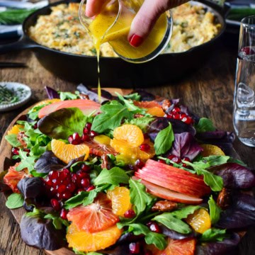 Drizzling salad dressing over a colourful Winter Citrus & Baby Green Salad