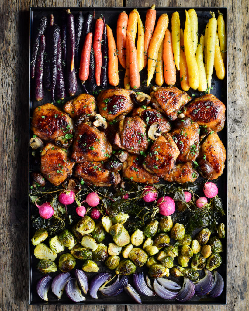A very colourful sheet pan of roasted vegetables and glazed chicken thighs.