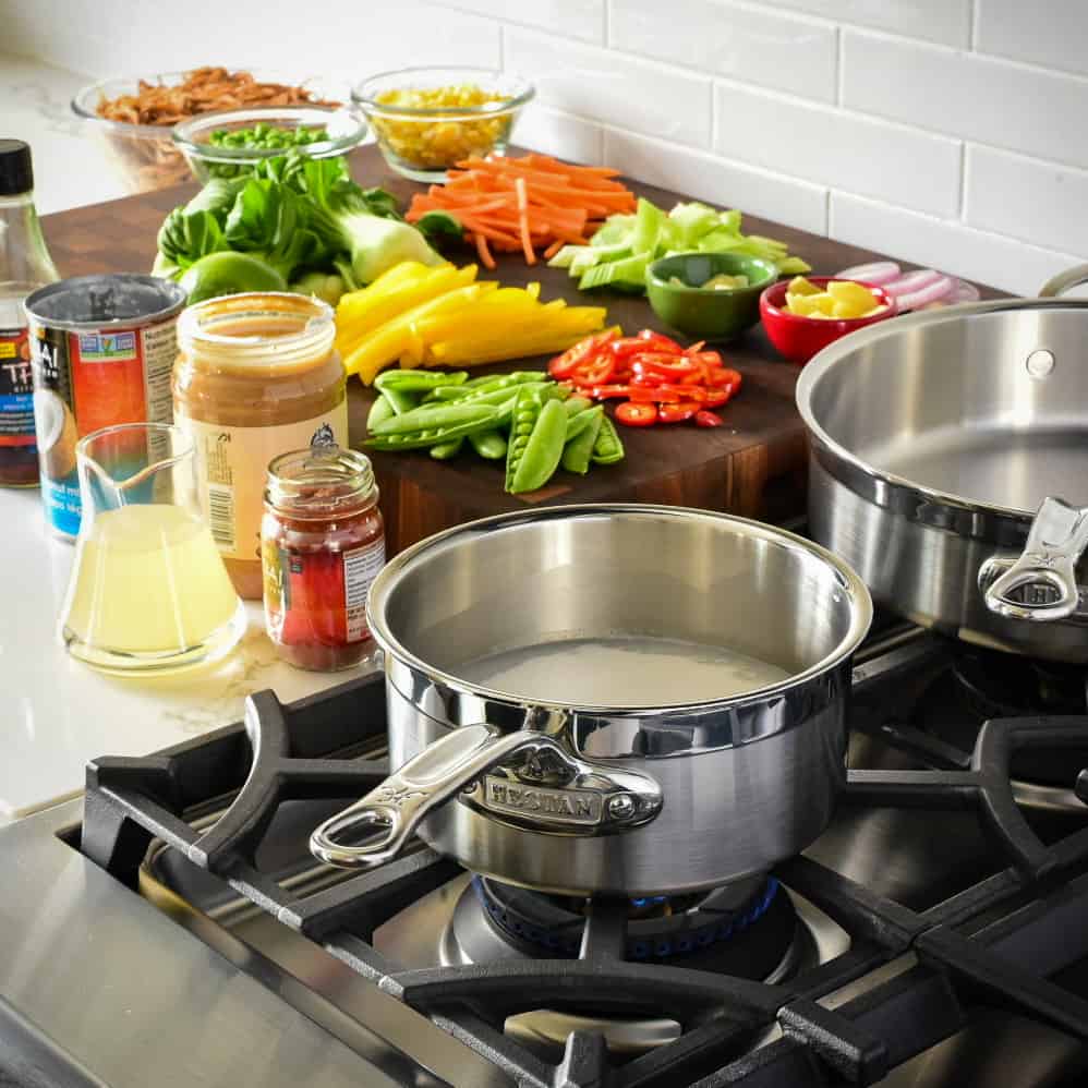 An image of two pans on the range with vegetables and other ingredients ready