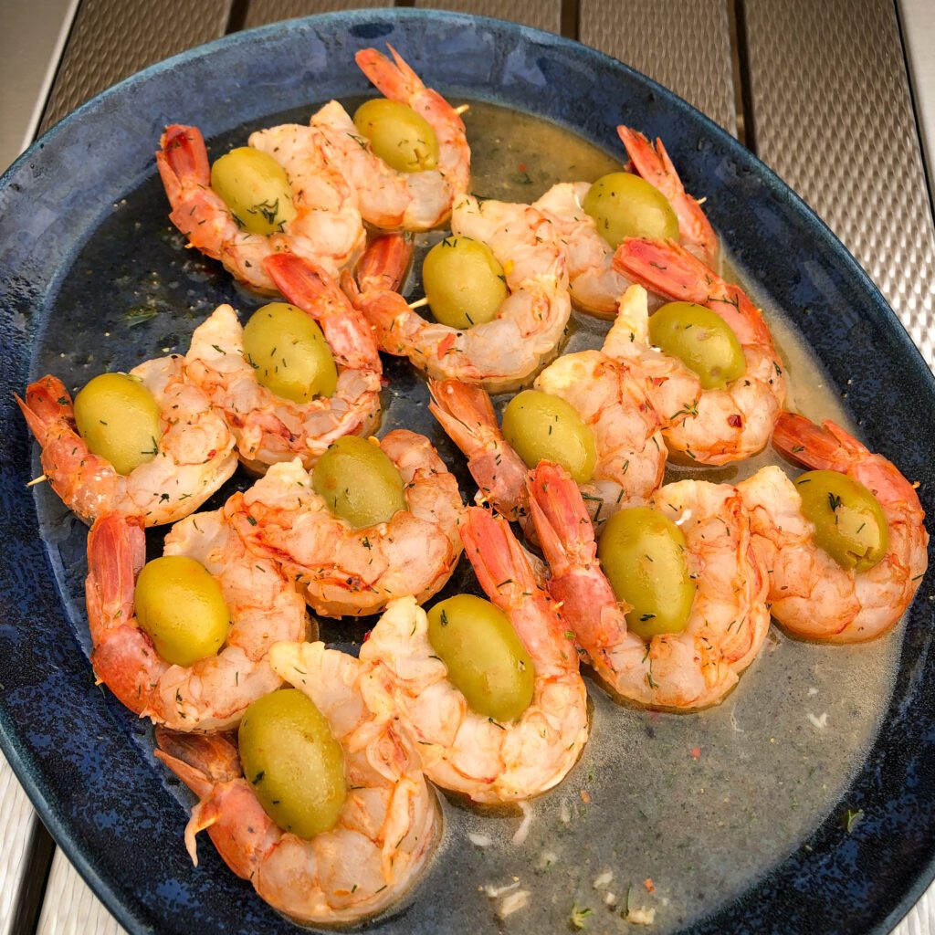 A blue oval plate with shrimp and olive skewers ready to go on the grill