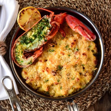 A small skillet with half a lobster sitting on a small skillet with mac and cheese.