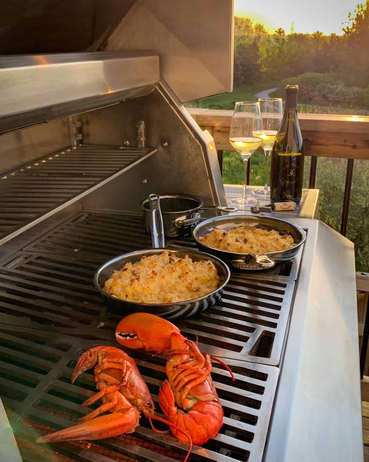 Two lobster halves and two skillets with mac & cheese on the grill.