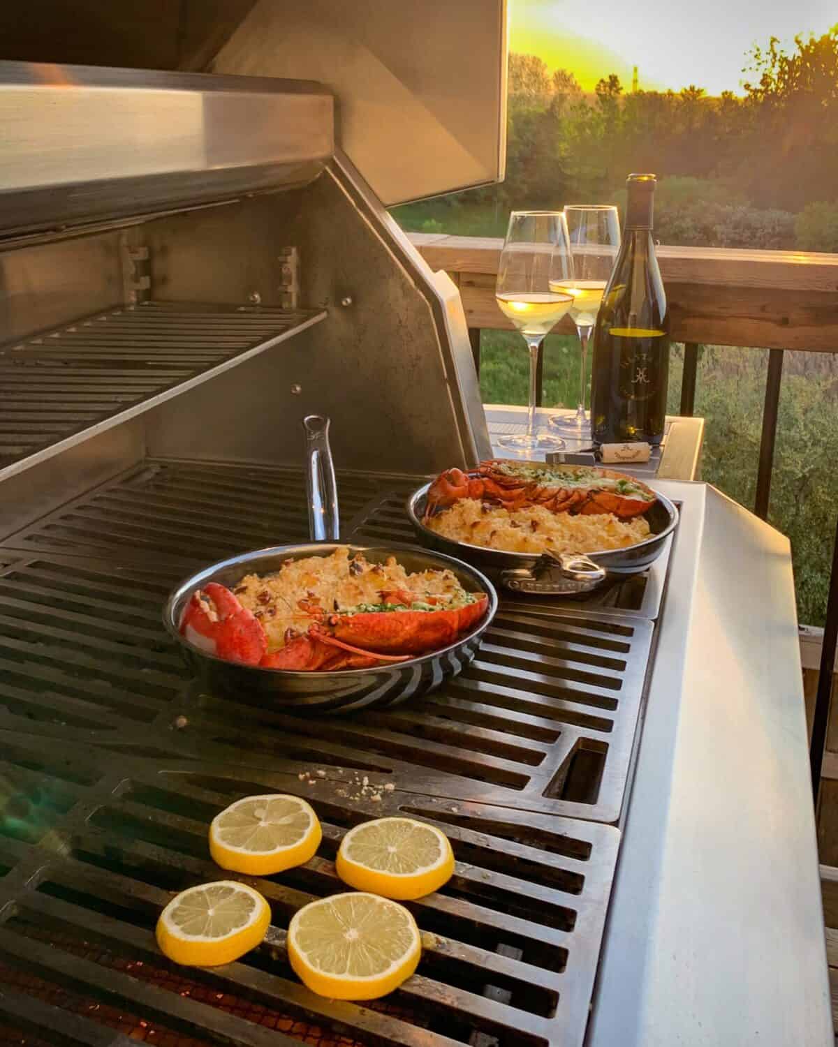 Two small skillets with grilled lobster halves on macaroni and cheese.
