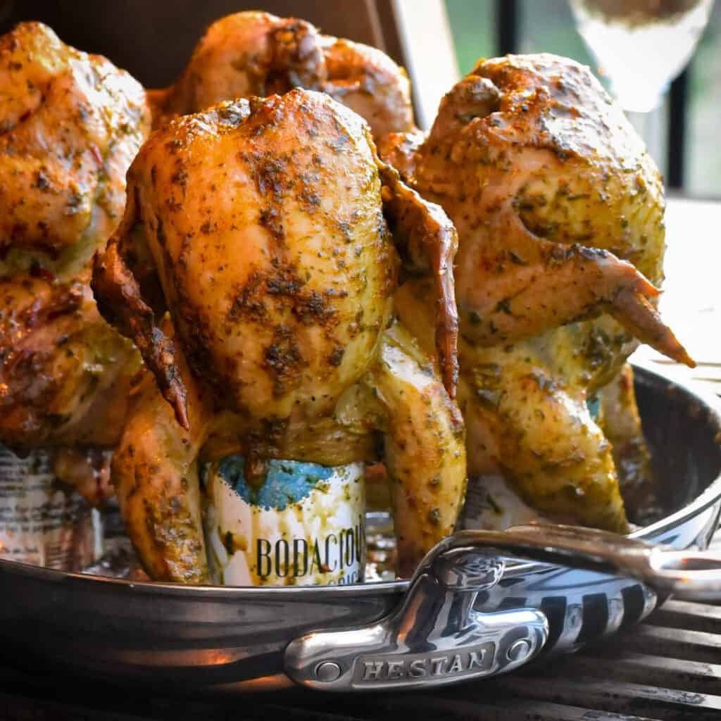 A close up of wine can cornish hens are placed on a skillet on a grill. The skin is crispy, golden brown.