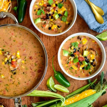 A pot and two bowls of Mexican Chicken and Corn Chowder surrounded by fresh corn, jalapeños and other toppings.