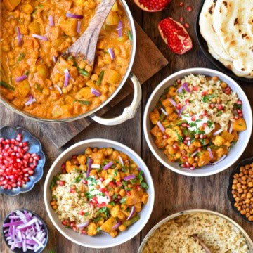 A pot of Roasted Butternut Squash, Cauliflower & Chickpea Curry with two bowls and toppings.