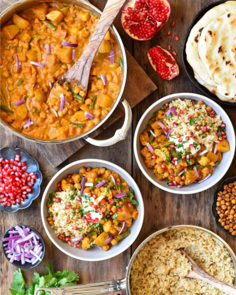 A pot of Roasted Butternut Squash, Cauliflower & Chickpea Curry with two bowls and toppings.