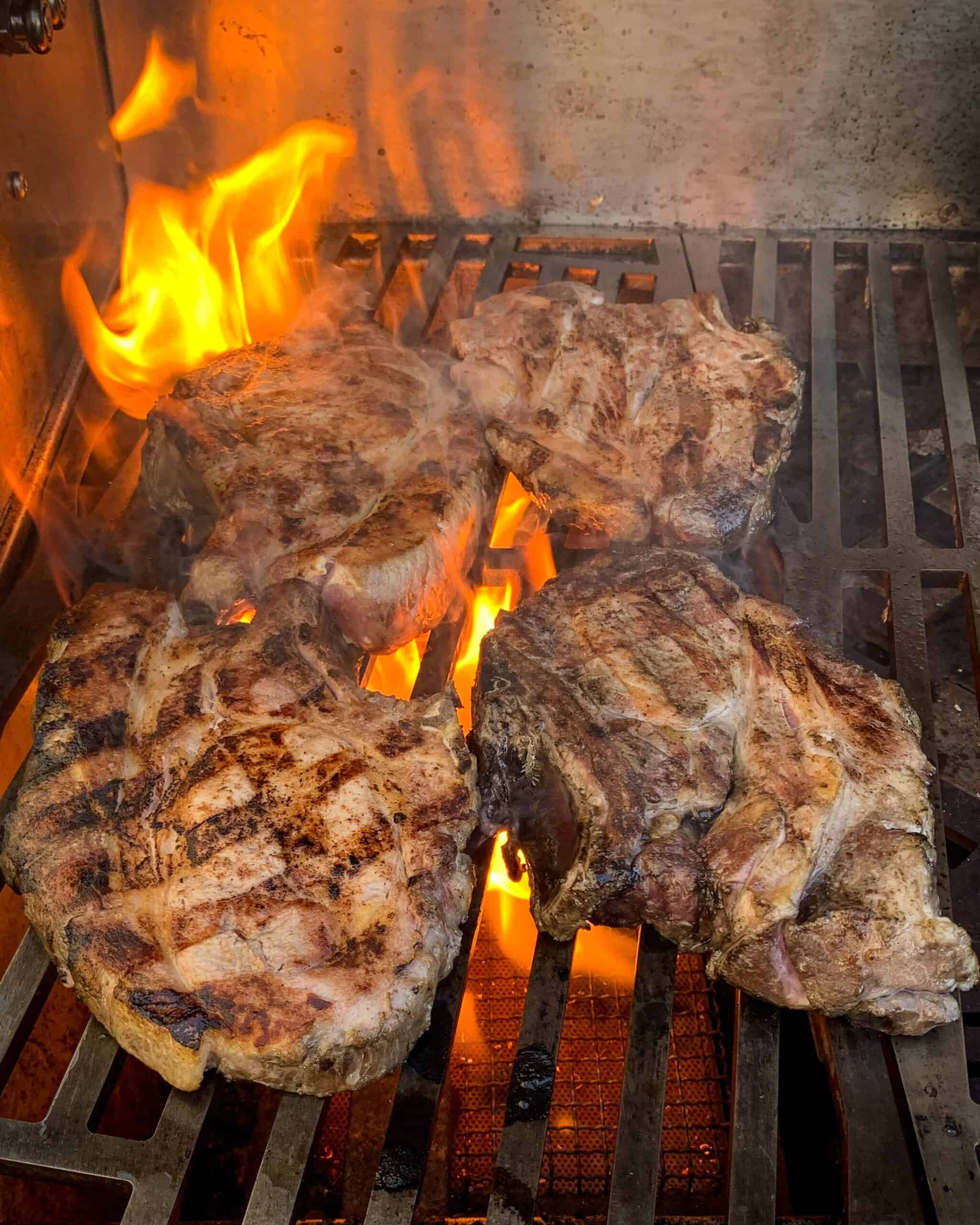 Four pork chops on a flaming hot grill
