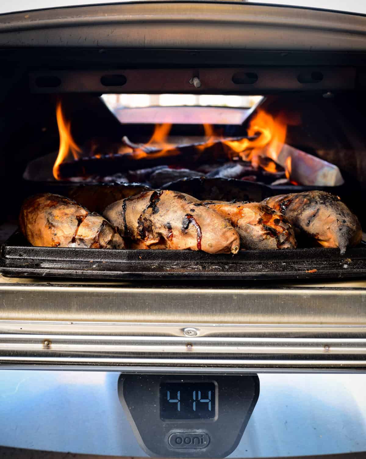 Baking sweet potatoes in a flaming wood oven with the fuel hatch opened.