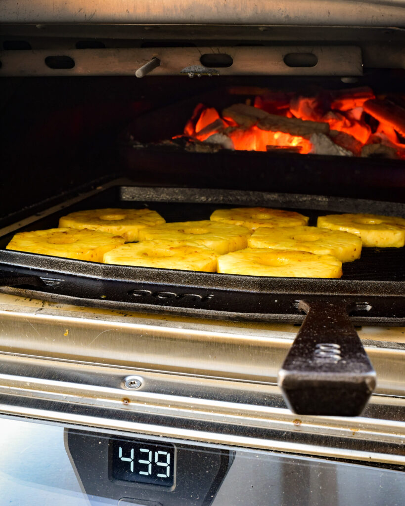 Pineapple slices on a cast iron pan in the pizza oven with glowing coals.