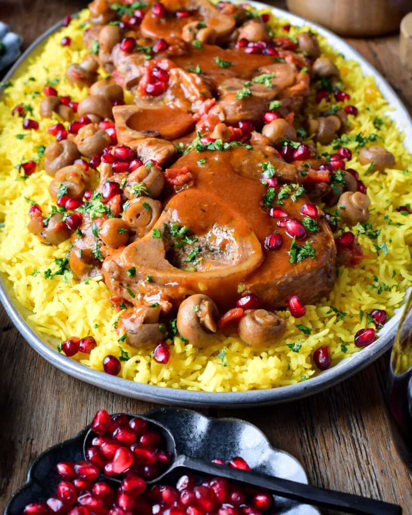 A platter of veal shanks with gravy over basmati rice. Sprinkled with pomegranates and parsley.