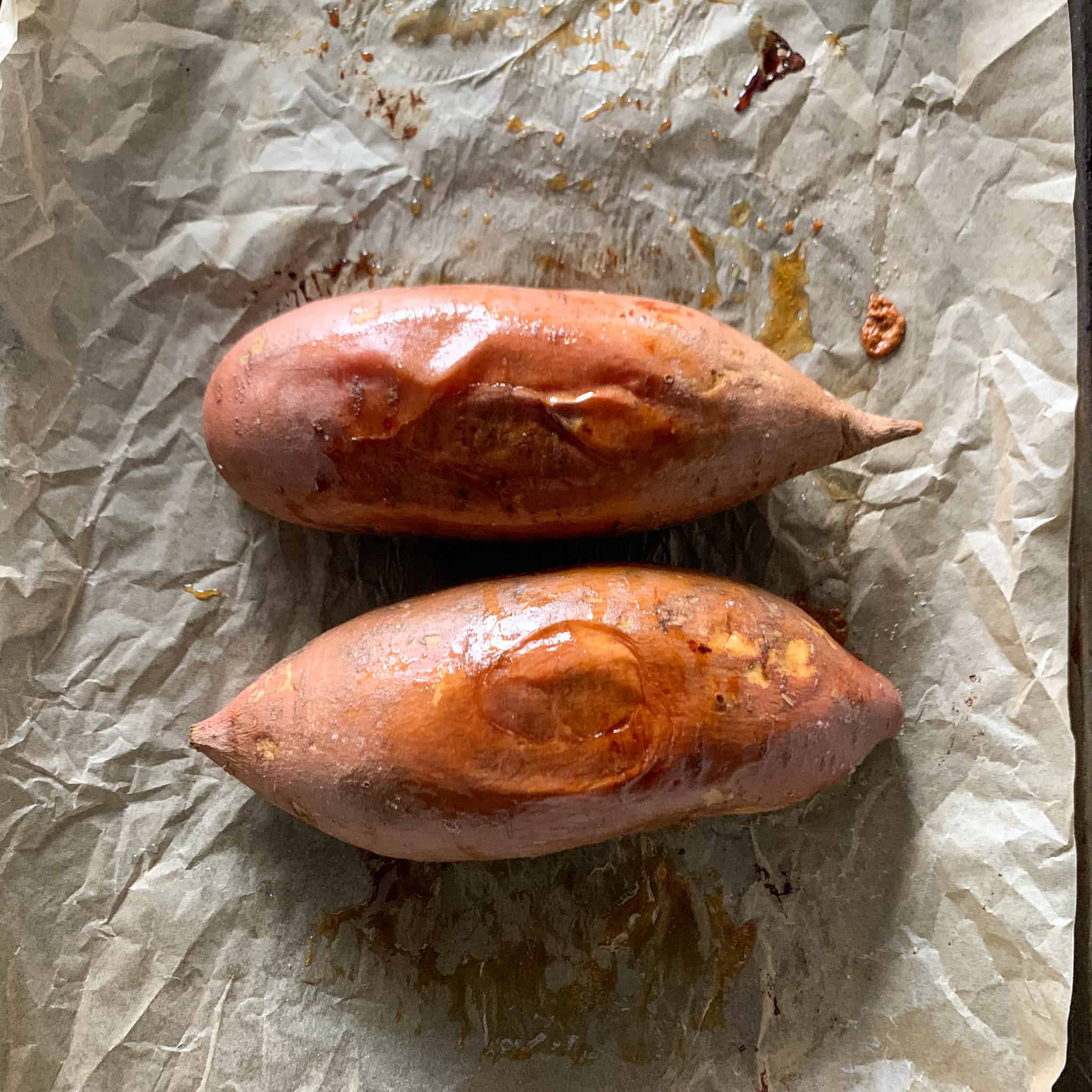 Two baked potatoes cooked on a baking sheet.