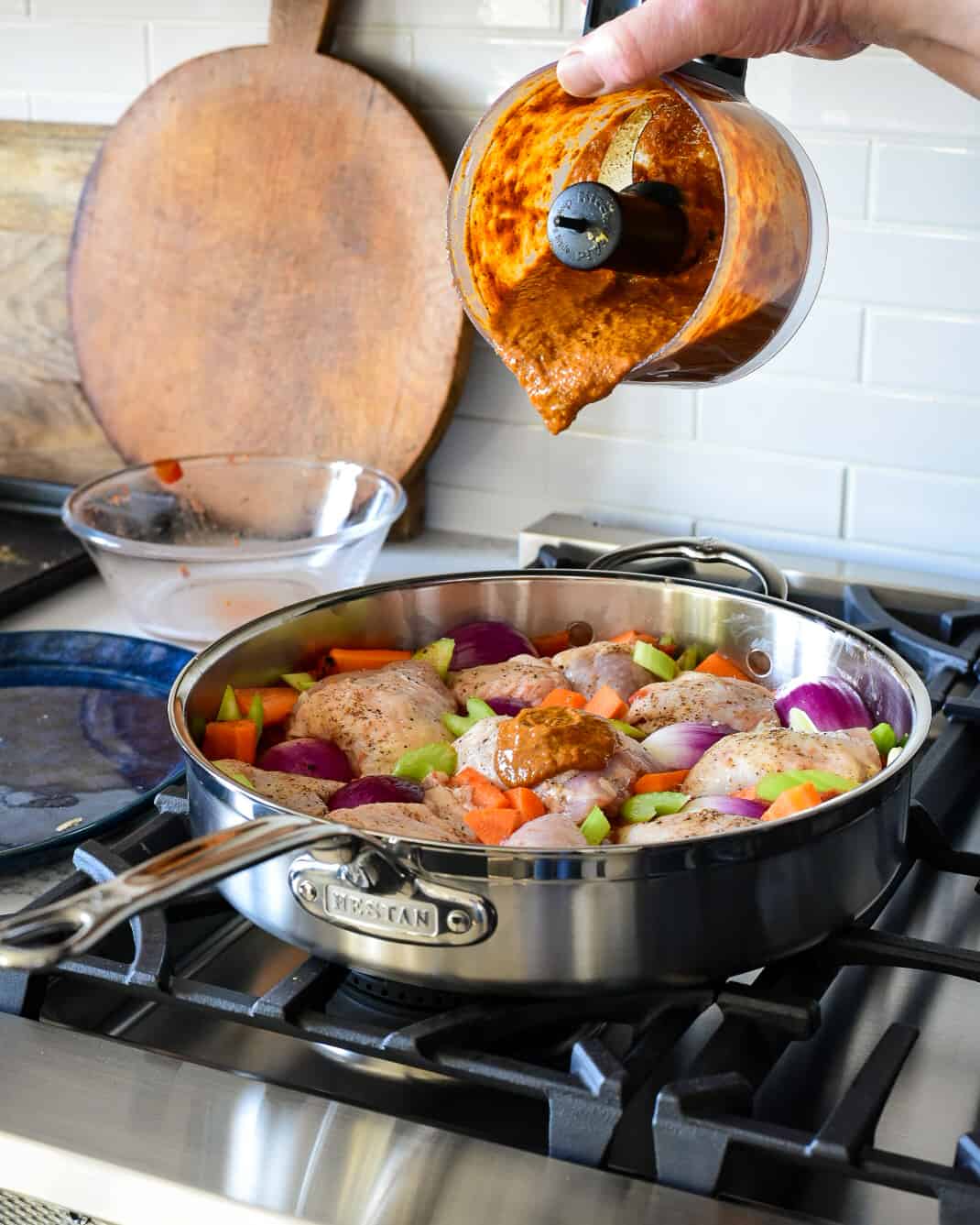 Sauce being poured on the baked Harissa Spiced Chicken dish before it goes into the oven.