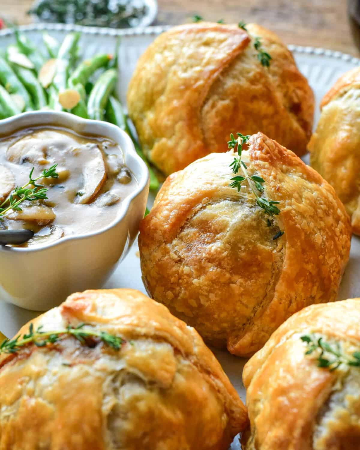 Close up image of the baked Wellington with a sprig of thyme beside a bowl of Marsala sauce.