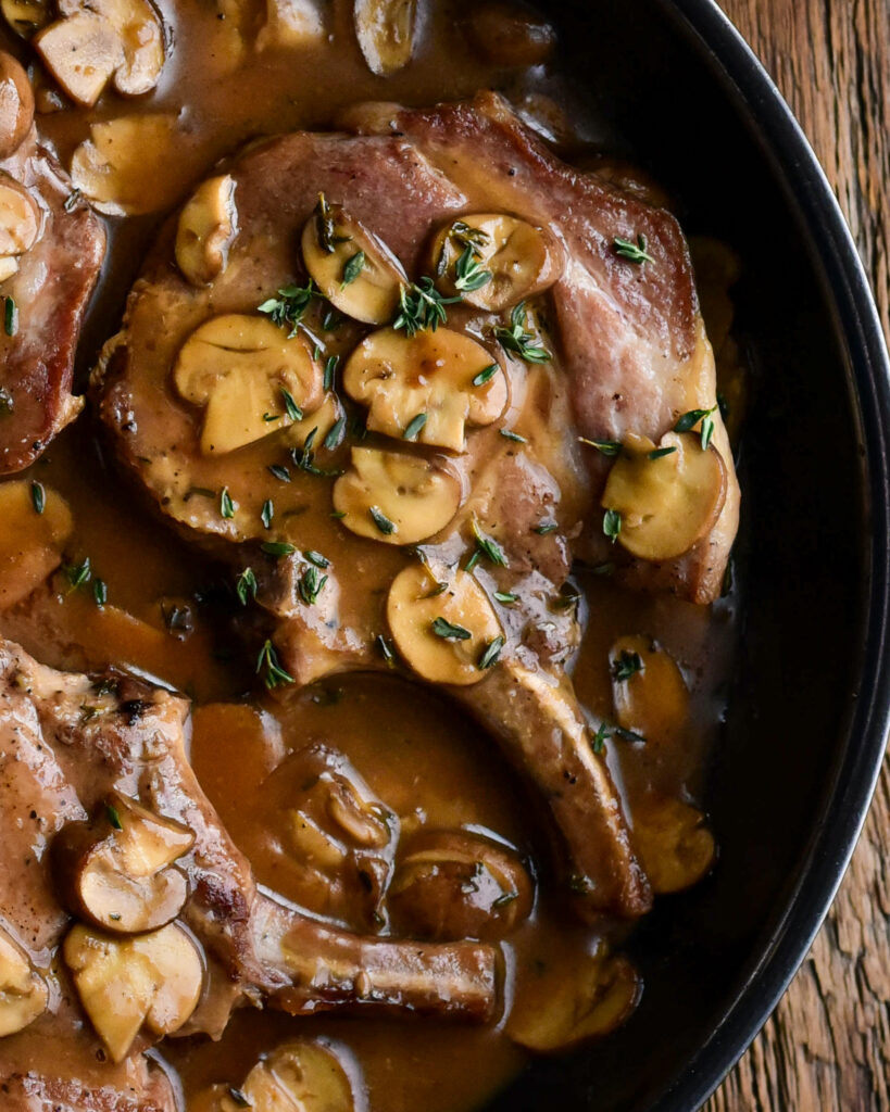 A close up of a pork chop in a pan filled with a creamy mushroom sauce.