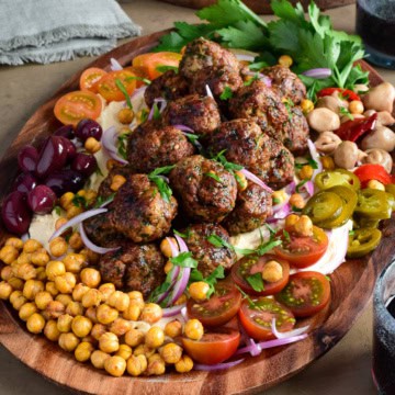 A platter of Loaded Hummus with Air Fryer Harissa Sausage Balls with a selection of fresh and pickled vegetables and herbs.