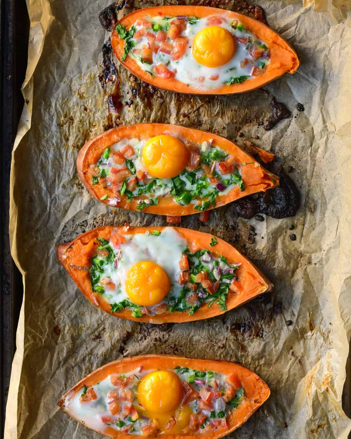 Four sweet potato boats with a cooked egg and vegetables.