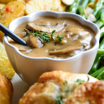 A bowl of Marsala mushroom sauce surrounded by individual ground beef wellingtons.