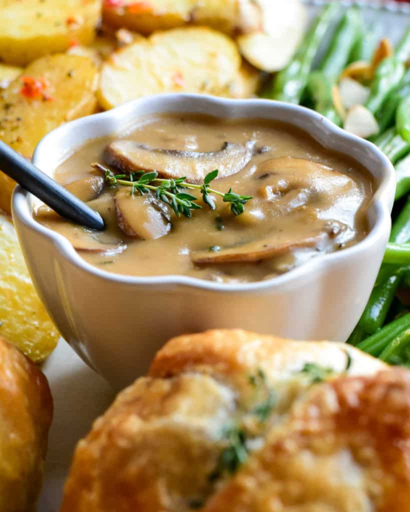A bowl of Marsala mushroom sauce surrounded by individual ground beef wellingtons.